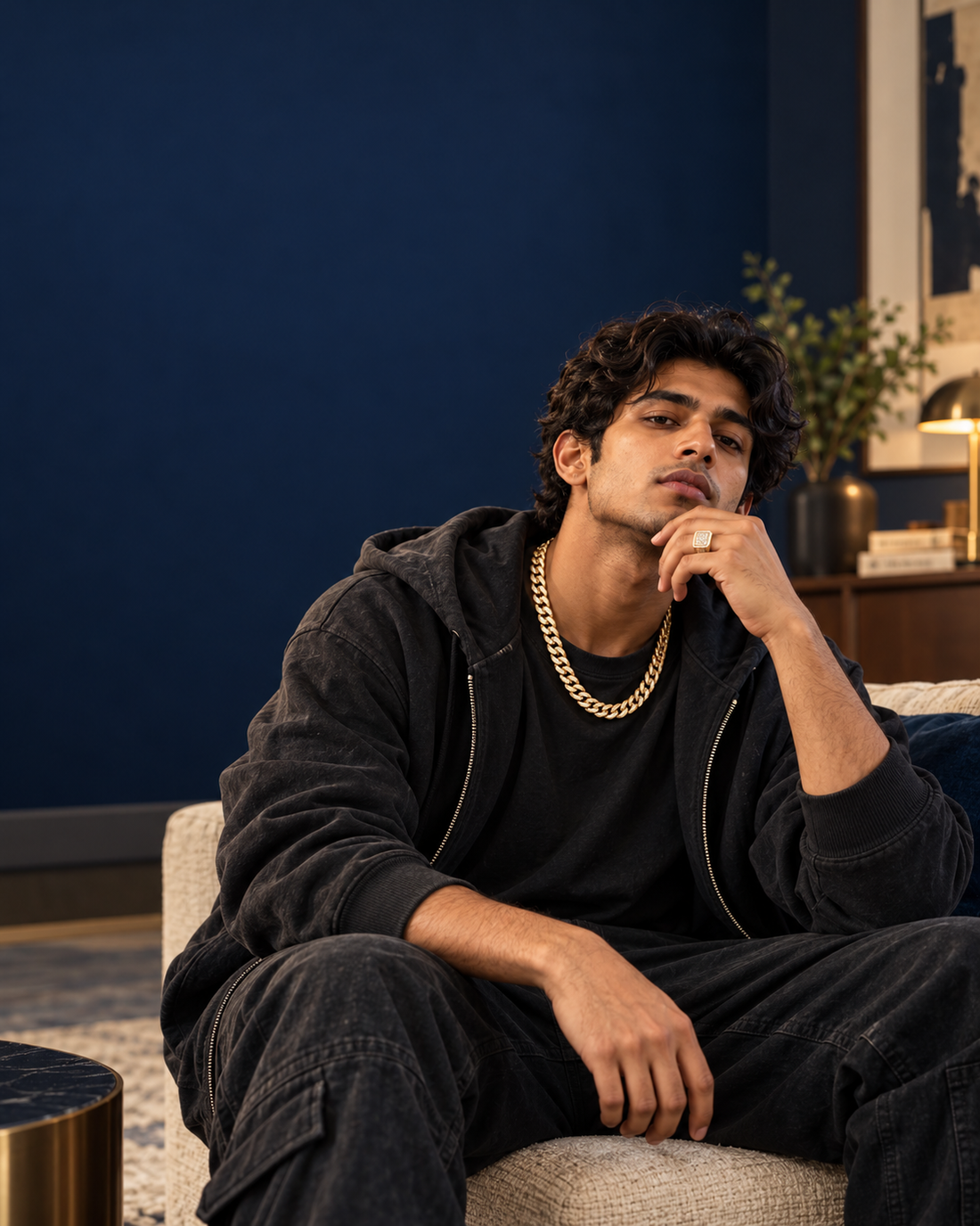 Indian man wearing a gold chain and ring in a dark navy lifestyle setting